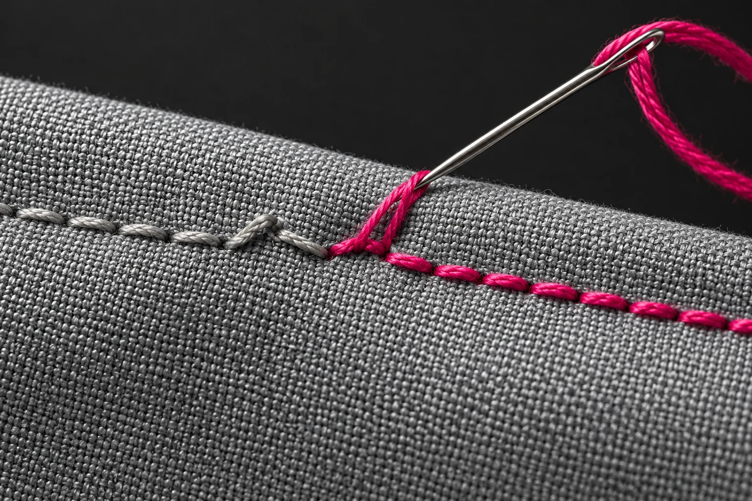 Detalle de costura gris con hilo fucsia y aguja, metáfora de corrección; ilustración IA.